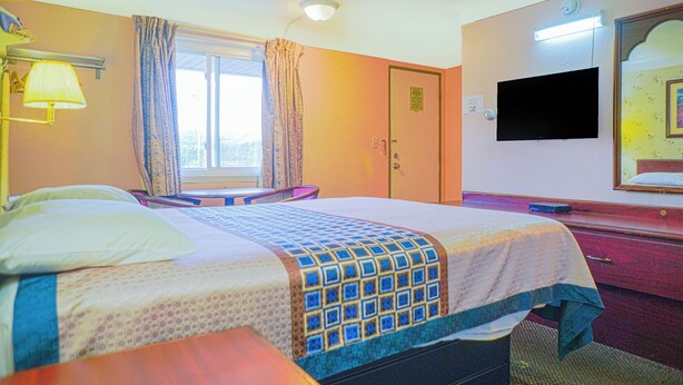 A hotel room with a bed, a desk, a chair, a television, and a bathroom with a mirror and sink.
