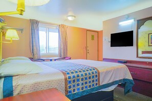 Une chambre d’hôtel comprenant un lit, un bureau, une chaise, une télévision et une salle de bain avec un miroir et un lavabo.