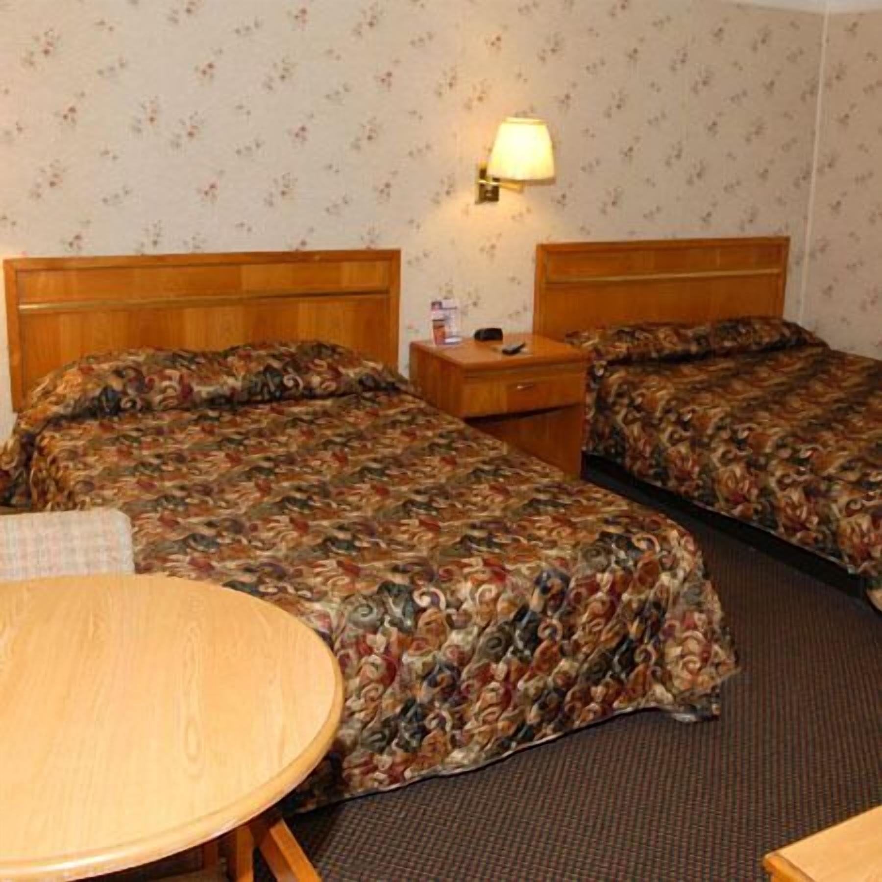 A hotel room with two beds, a nightstand, a table, and a wall-mounted lamp.