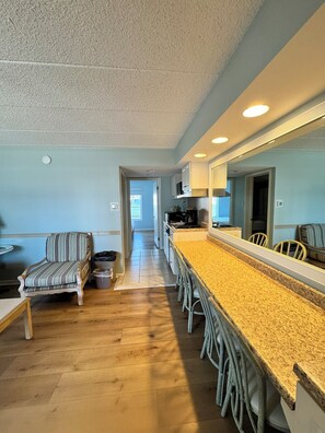A modern kitchen with a long island, wooden flooring, and a striped chair. - Wild Dunes Inn (Ocean City)