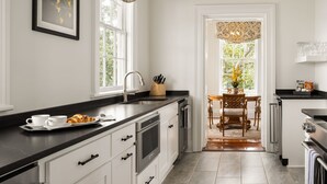 A modern kitchen with white cabinets, a black countertop, and a dining area with a wooden table and chairs. - The Jasmine House (Charleston)