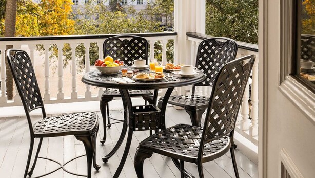 A balcony with a table set for breakfast, featuring fruits, bread, and beverages. - The Jasmine House (Charleston)