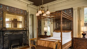 A four-poster bed with a wooden frame and a bench, a fireplace, a large mirror, and a chandelier. - The Jasmine House (Charleston)