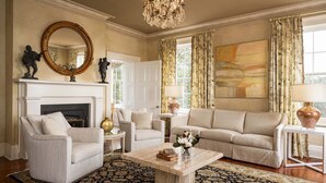 A living room with a fireplace, two armchairs, a sofa, a coffee table, and a chandelier. - The Jasmine House (Charleston)
