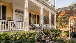 A historic building with a covered porch, columns, and a staircase leading to the entrance. - The Jasmine House (Charleston)