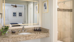 A bathroom with a granite countertop, a sink, a mirror, framed artwork, and a shower area.