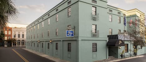 A light green building with a blue sign, a black awning, and a flag.