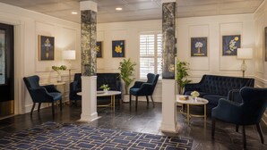 A lobby with dark wood flooring, blue upholstered chairs, a dark blue sofa, and a patterned rug.