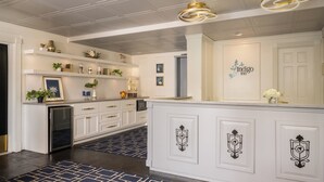 A hotel reception area with a white reception desk, a refrigerator, and a blue patterned rug.
