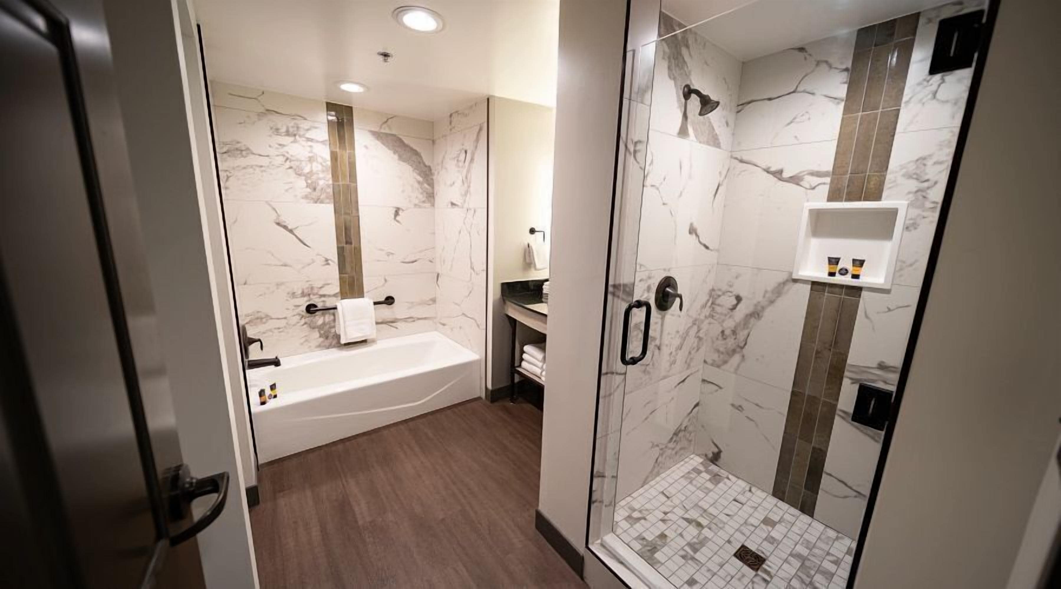 Un baño moderno con ducha de mármol, bañera y zona de ducha con paredes de vidrio.