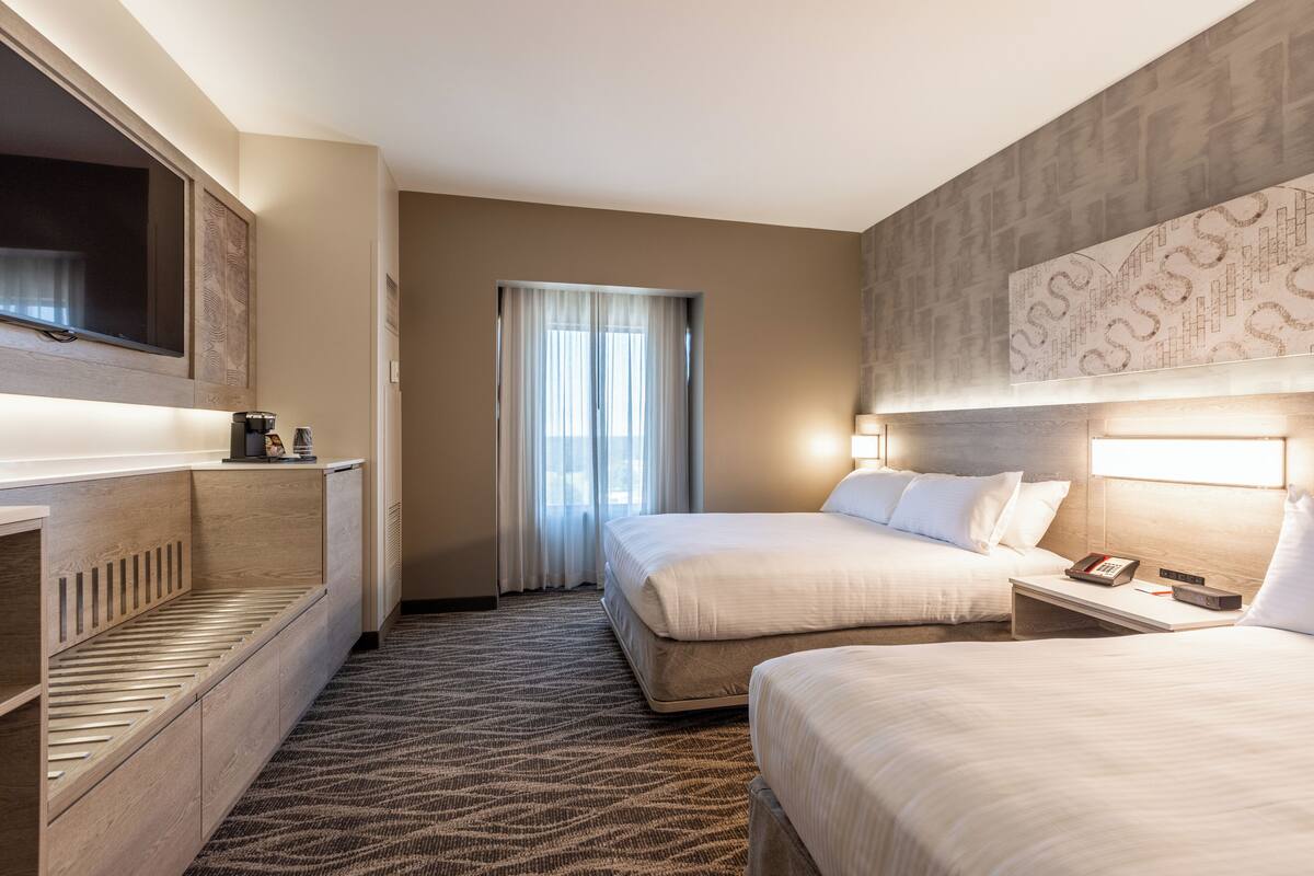A hotel room with two beds, a desk, a television, and a window with curtains.