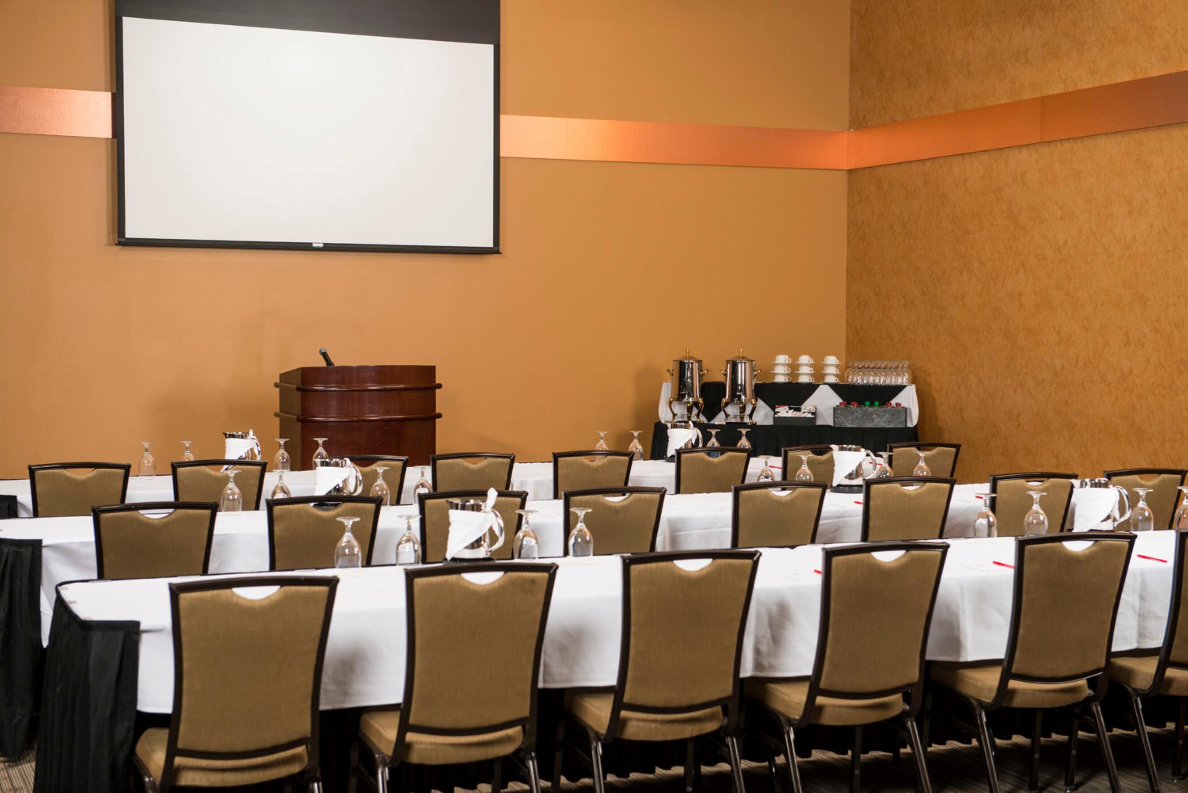 A conference room with multiple tables and chairs, a projector screen, and a coffee station.
