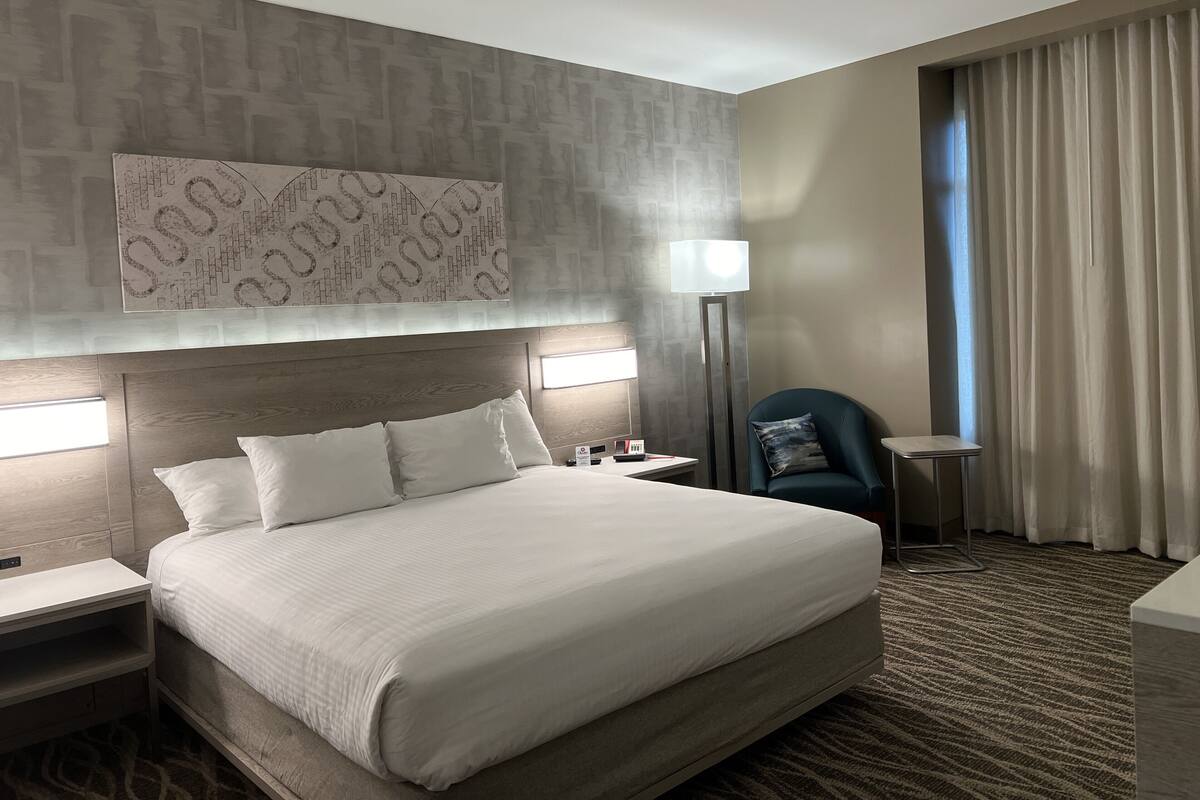 A hotel room with a large bed, two bedside tables, a chair, a floor lamp, and a large abstract artwork on the wall.