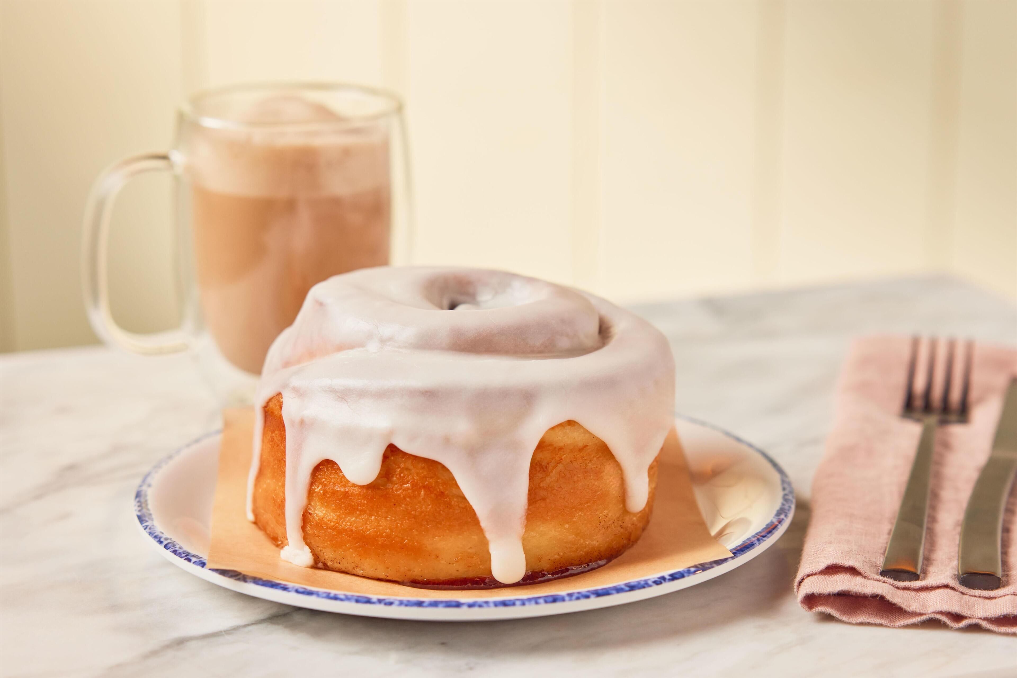 A glazed donut on a plate with a napkin and fork beside it.