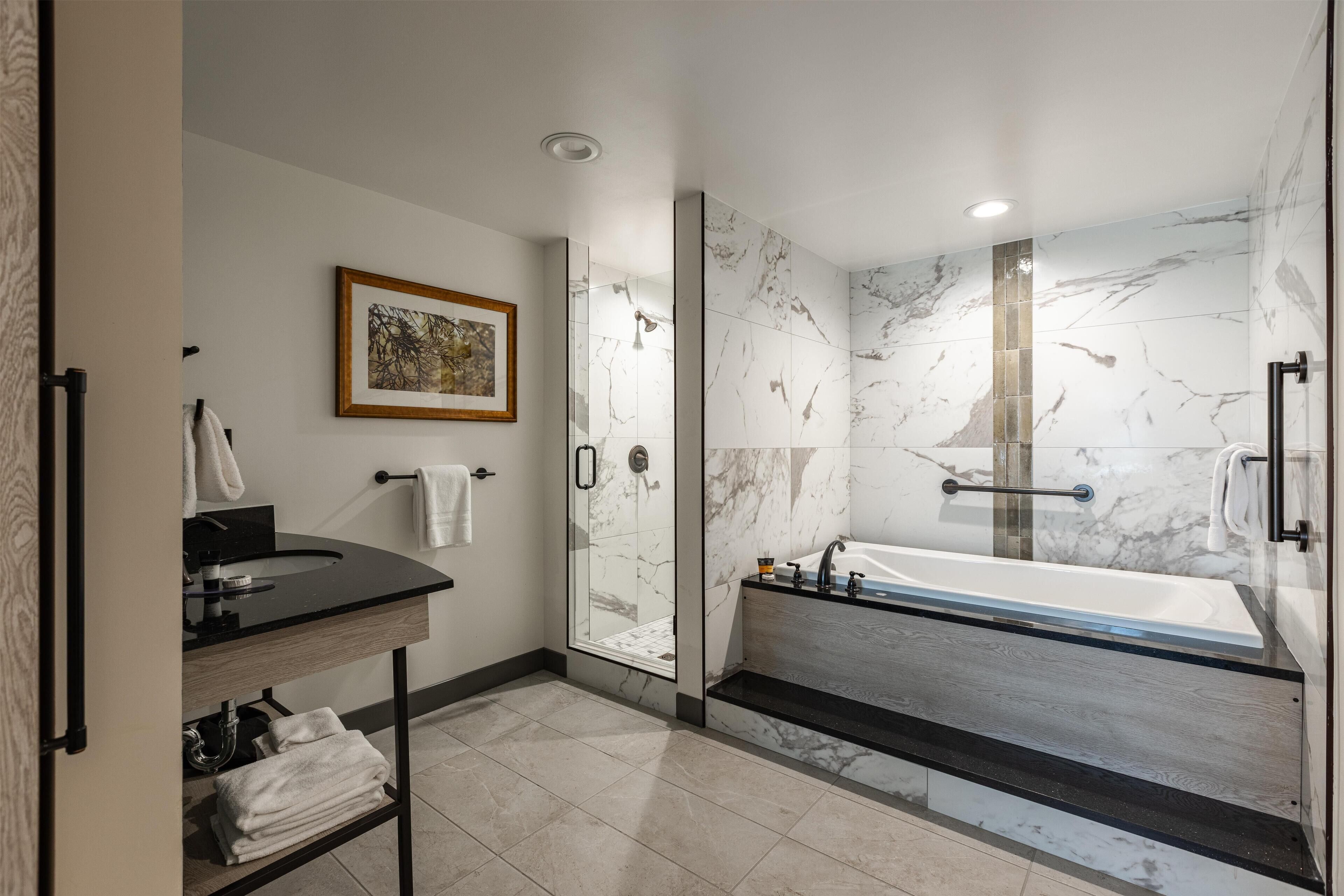 A modern bathroom with a glass-enclosed shower, a freestanding bathtub, and a vanity with a sink and towel rack.