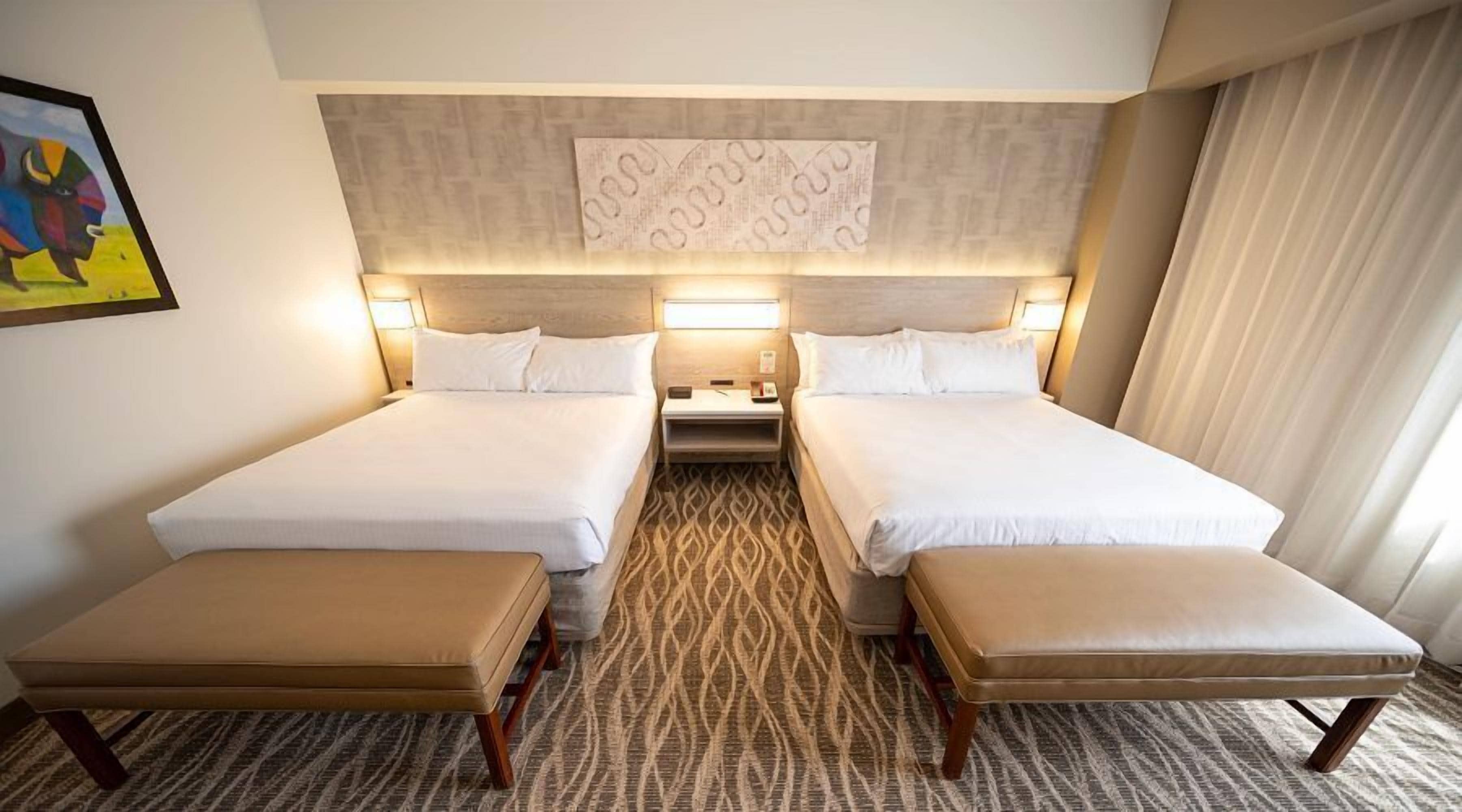 Une chambre d’hôtel avec deux lits, une petite table et un banc.