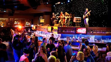 Un bar con escenario para música en vivo, una multitud de personas y diversas botellas en estanterías.
