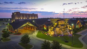 A hotel with a large building in the background, a landscaped area with a waterfall feature, and a parking lot. - Cherokee Casino & Hotel West Siloam Springs (Colcord)