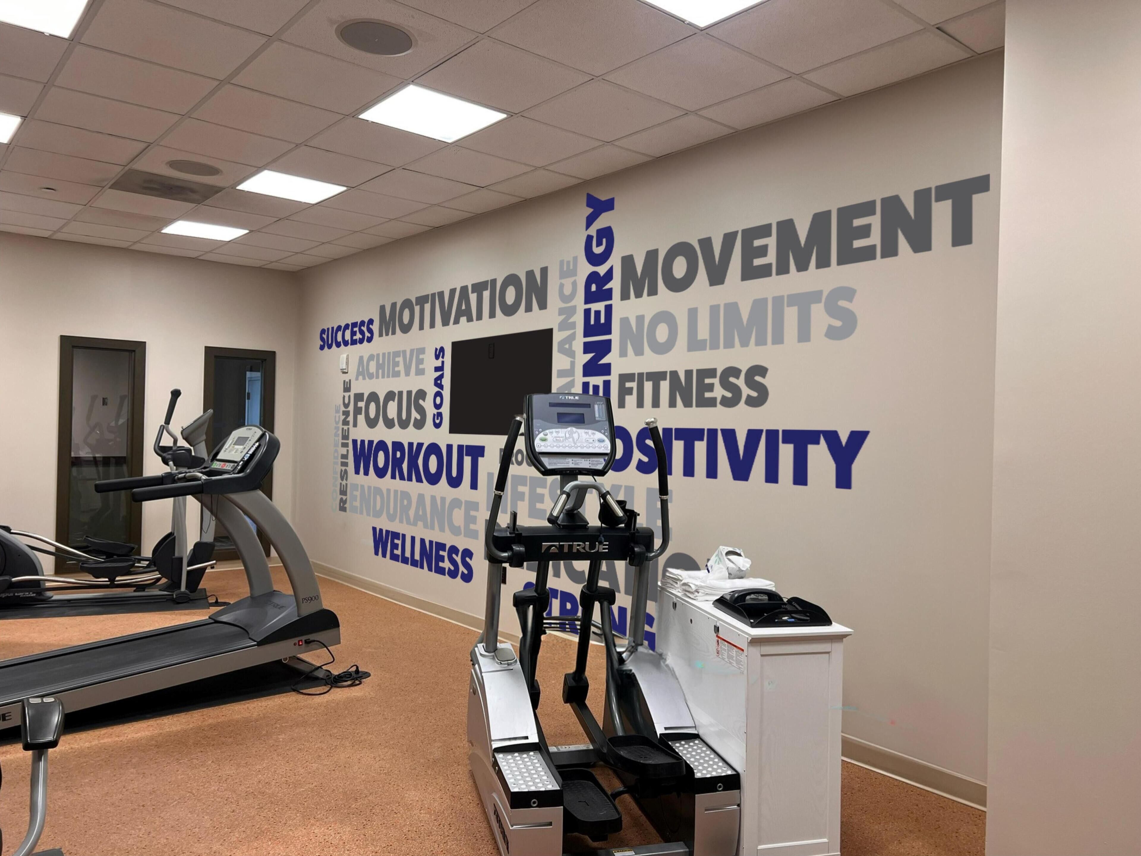 A gym with treadmills and an elliptical machine, a wall with motivational words, and a white cabinet with a scale.