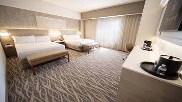 A hotel room with two beds, a desk, a chair, and a large window with curtains.