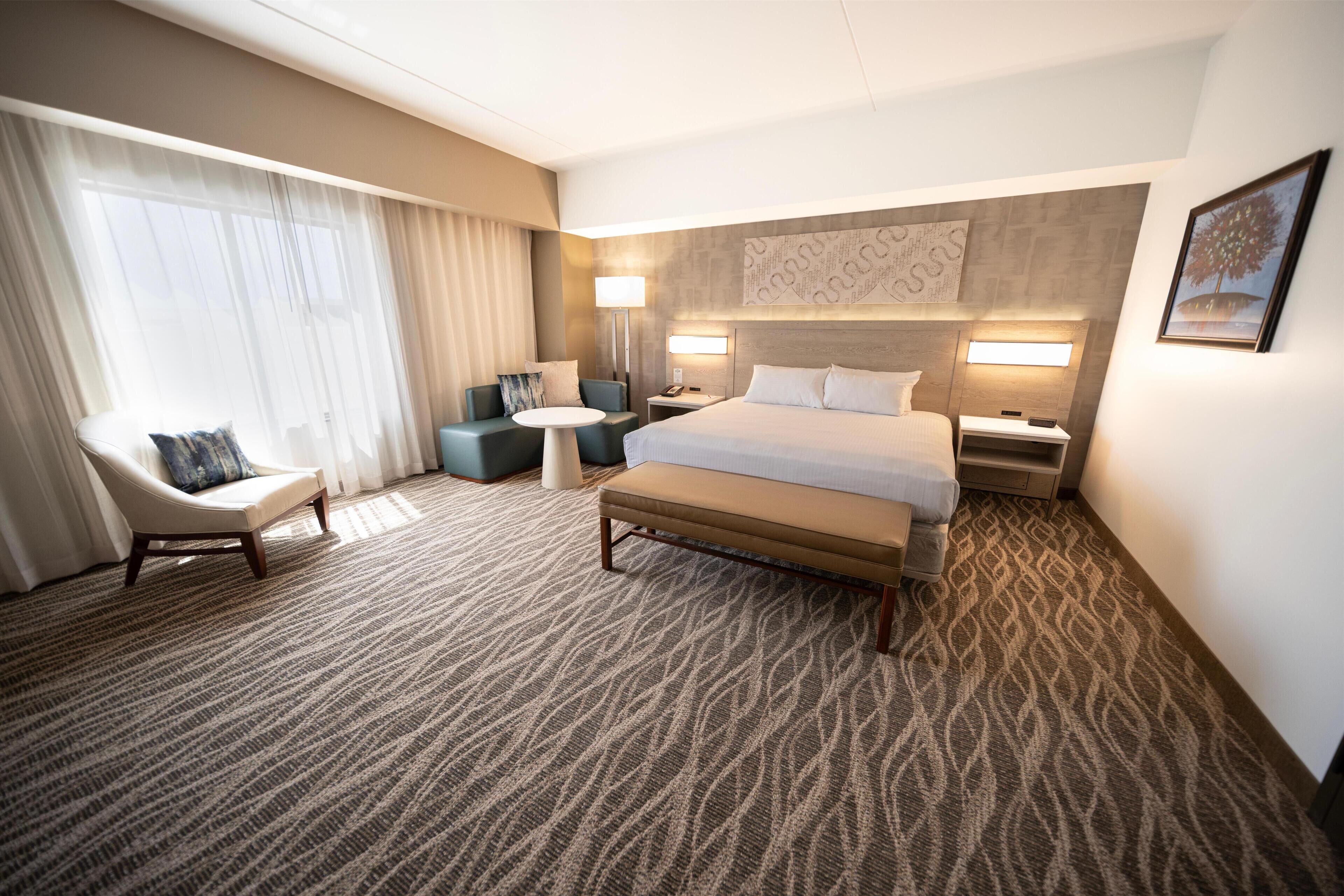 A hotel room with a large bed, a desk, a chair, and a small table.