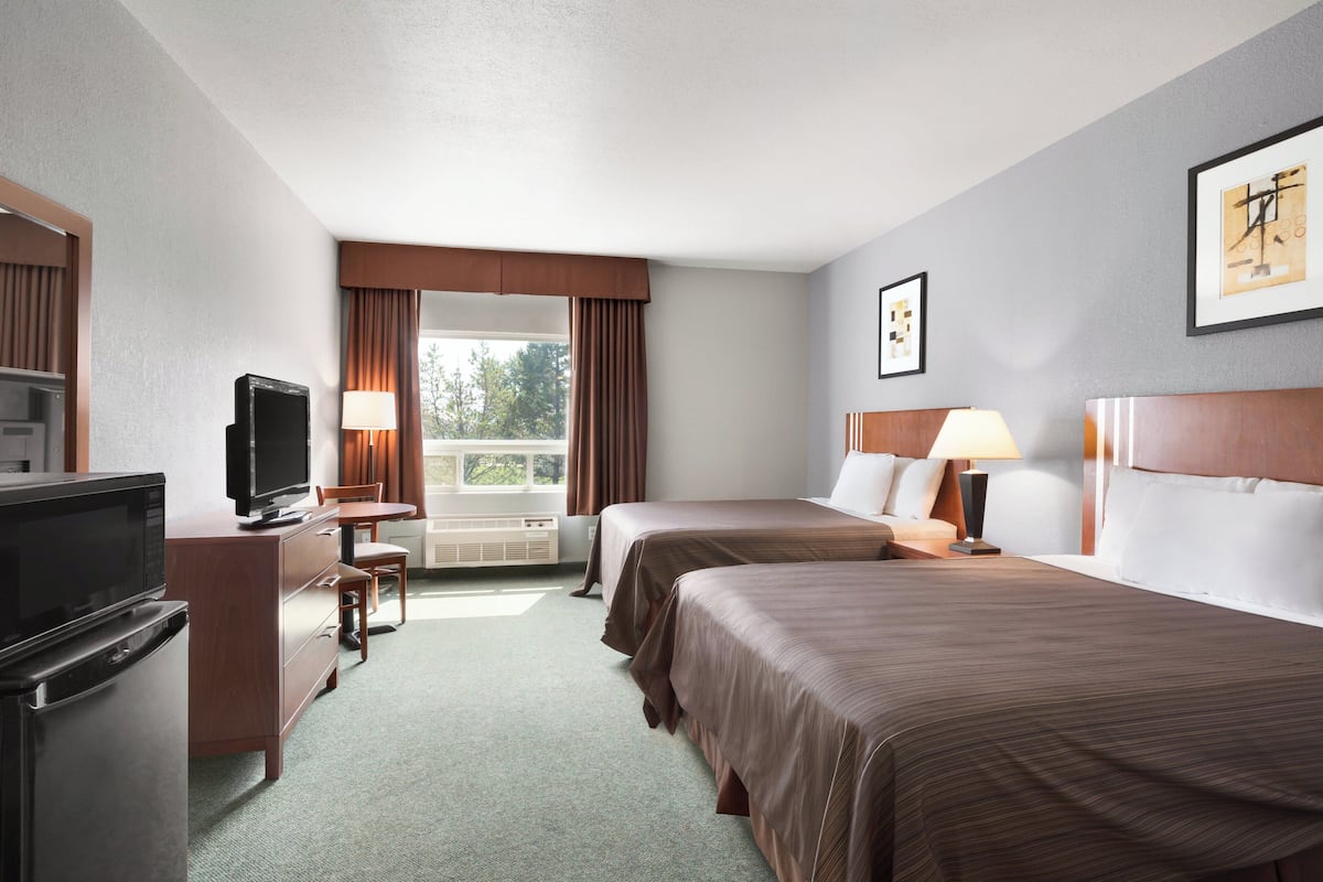 A hotel room with two beds, a TV, a desk, and a window with curtains.