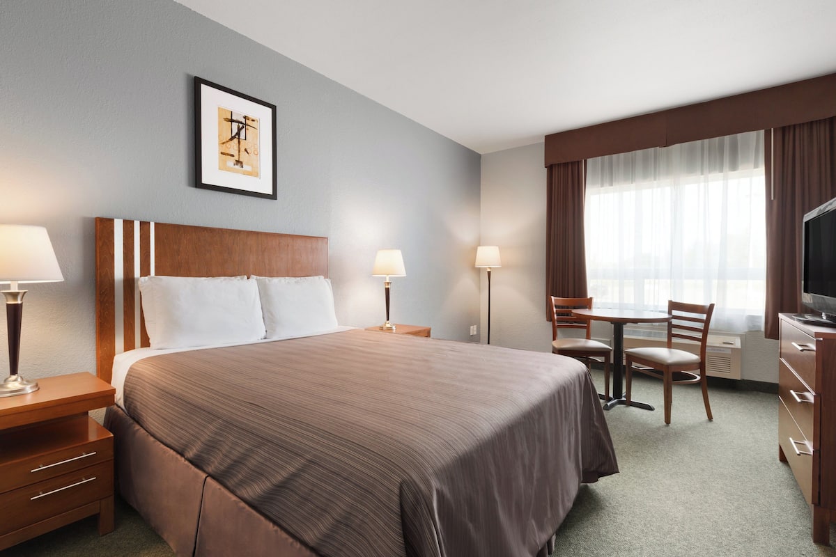 A hotel room with a large bed, two bedside tables with lamps, a desk with a chair, a television, and a framed picture on the wall.
