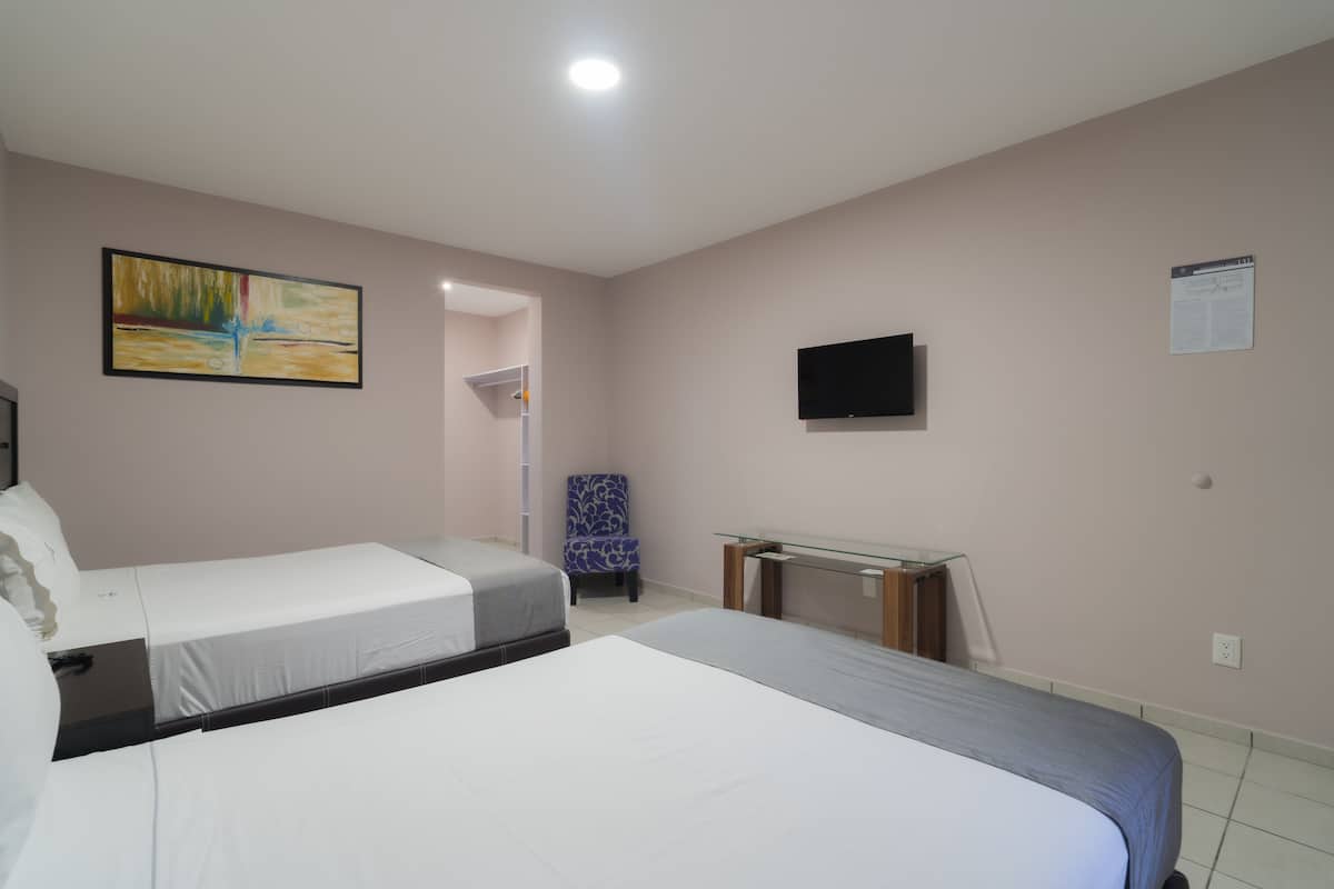 A hotel room with two beds, a desk, a chair, a TV, and a painting on the wall.