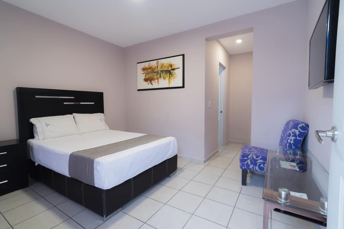 A bedroom with a bed, a chair, a TV, and a painting on the wall.