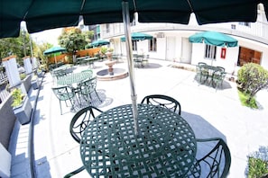 Un'area patio esterna con tavoli e sedie rotonde, ombrelloni e piante in vaso.
