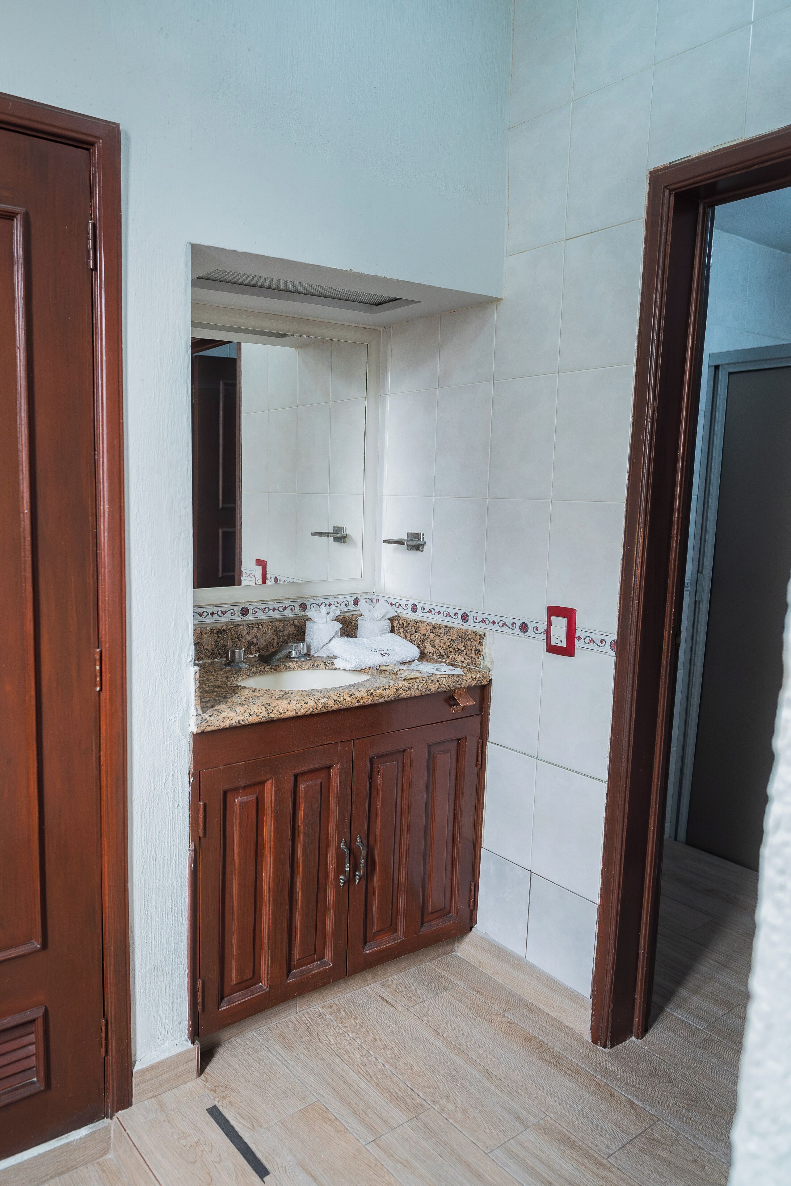 Un baño con tocador de madera, espejo y pared con azulejos.