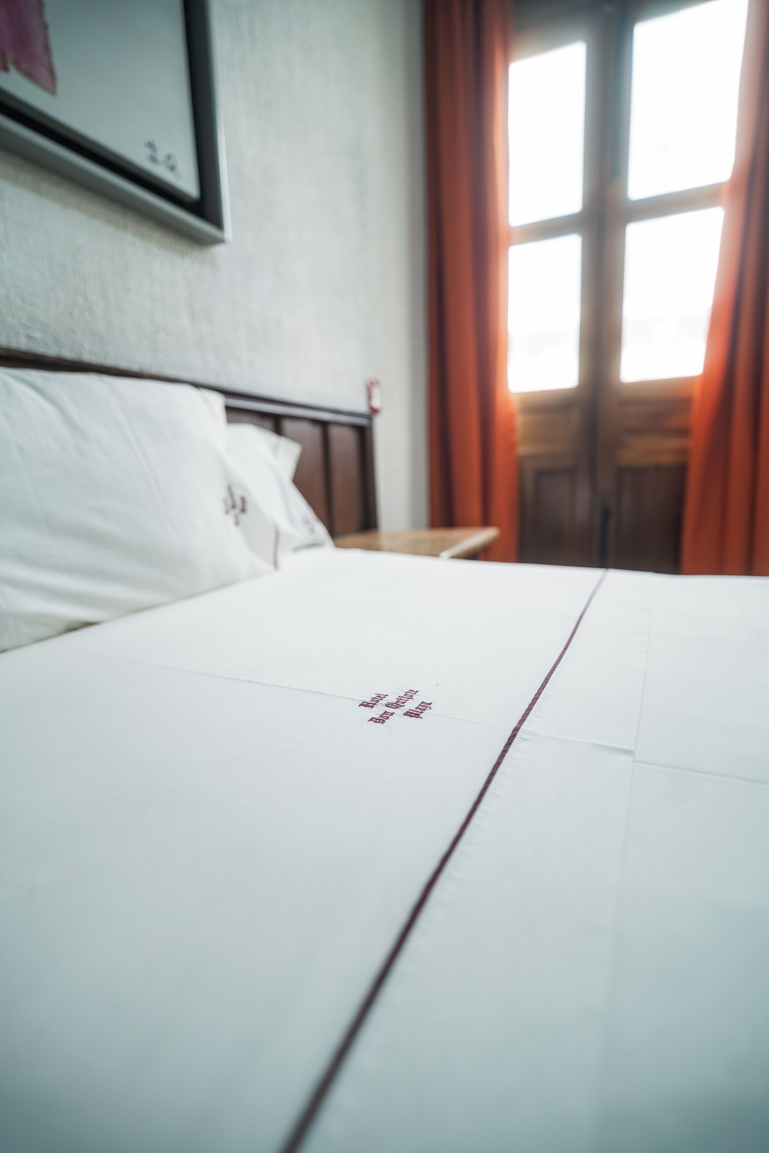 Una cama bien hecha con sábana blanca y texto bordado en rojo.