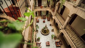 A courtyard with a fountain, potted plants, and wooden furniture.