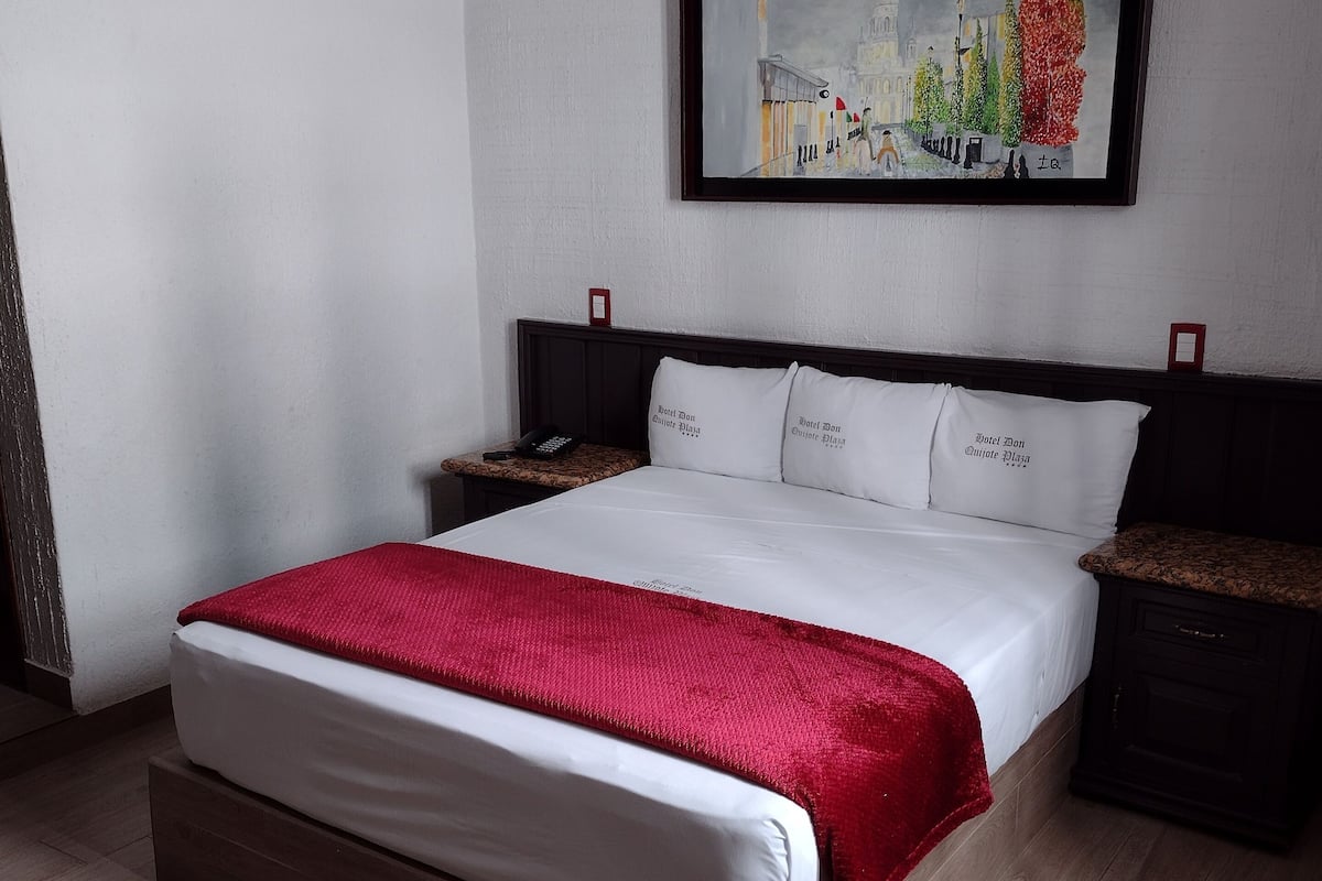 Une chambre d’hôtel avec un grand lit, une table de chevet, une commode, un tableau encadré au mur et un plancher en bois.