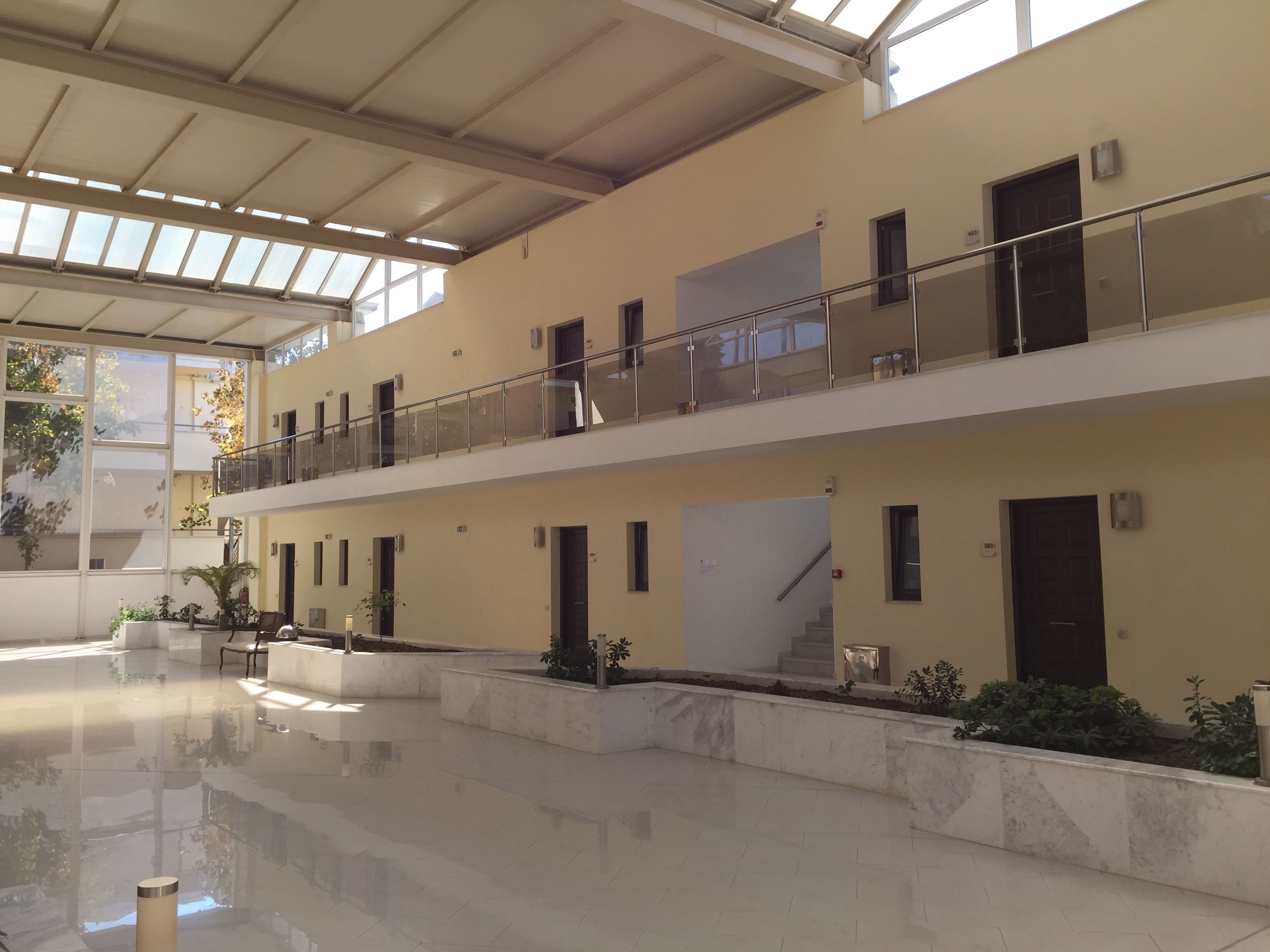 A spacious, multi-level atrium with a polished floor, large windows, and a balcony with glass railings.