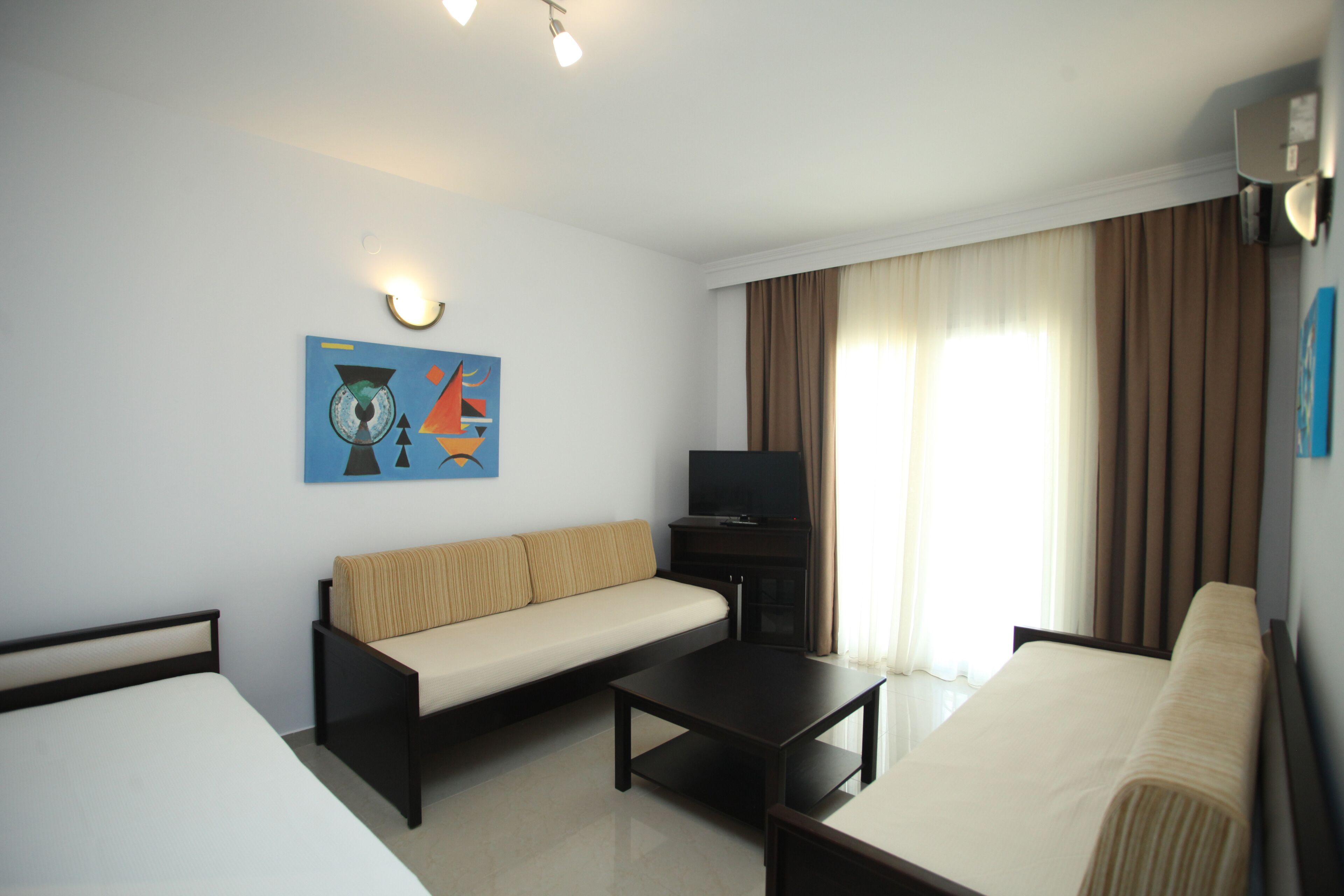 A hotel room with a bed, a sofa, a TV, and a painting on the wall.