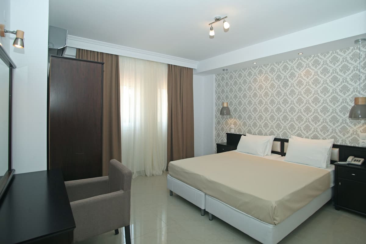 A hotel room with a bed, bedside tables, a desk, a chair, and a wardrobe.