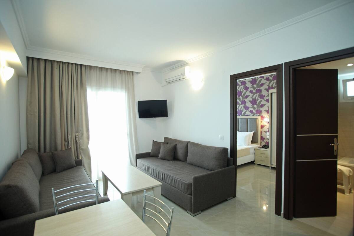 A modern hotel room with a sofa, a dining table, and a TV.