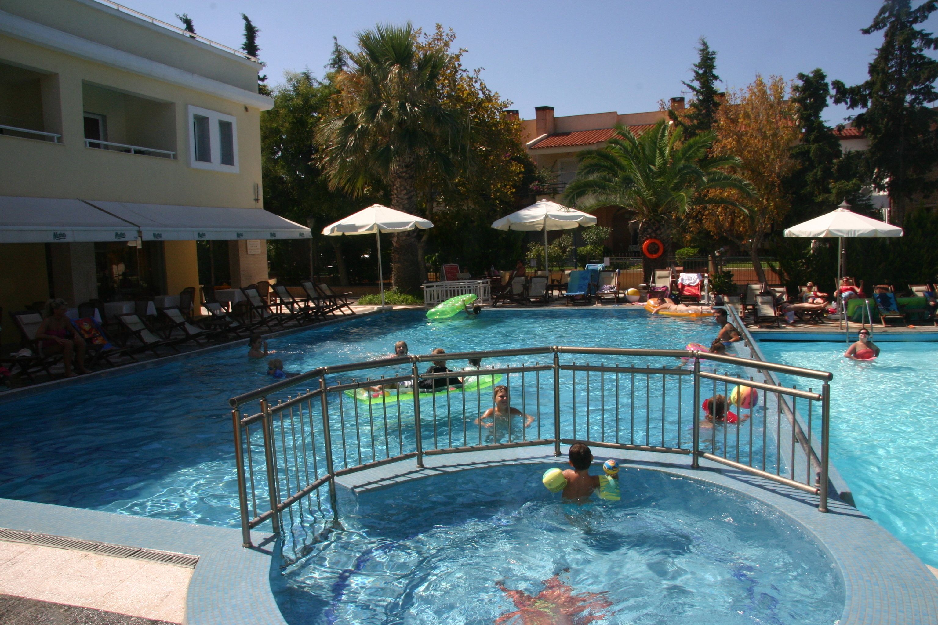 Un espace piscine comprenant plusieurs piscines, des chaises longues, des parasols et un bâtiment doté d’un balcon.