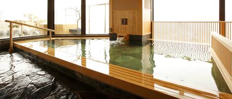 A traditional Japanese onsen with a wooden interior, stone flooring, and large windows allowing natural light.