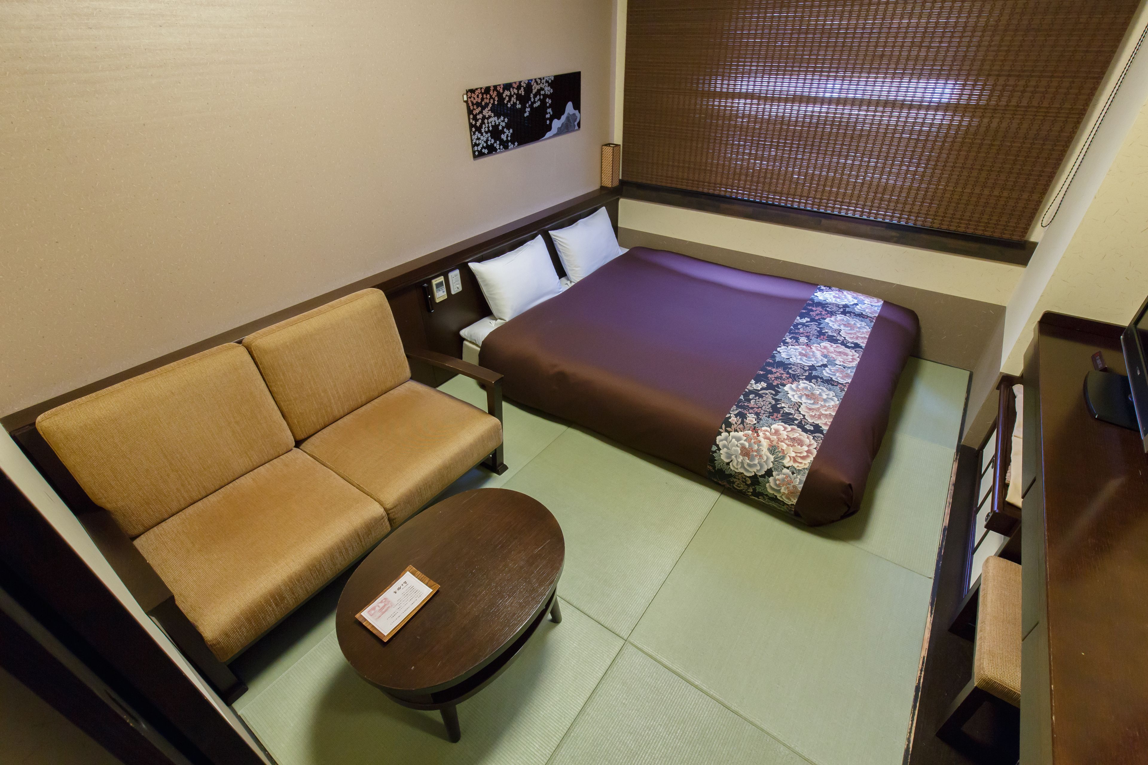Quarto de hotel com cama, sofá, mesa pequena e televisão na parede.