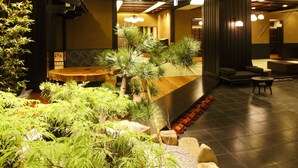 Un vestíbul amb taulell de recepció, zona de seients i un petit jardí interior amb plantes i pedres.