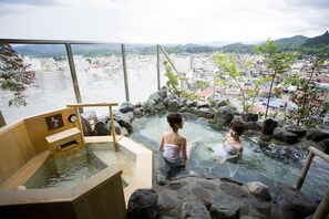 A hot spring bath with wooden benches and a view of a cityscape through large windows. - Hida Hanasatonoyu Takayama Ouan (Takayama)