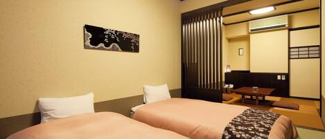 A hotel room with two beds, a small table, a chair, a wall-mounted air conditioner, and a sliding door.