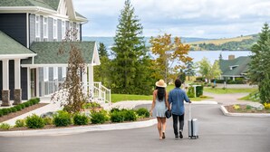 Un couple se promène dans une rue résidentielle devant une maison dotée d’un toit végétalisé, de boiseries blanches et offrant une vue sur un lac.
