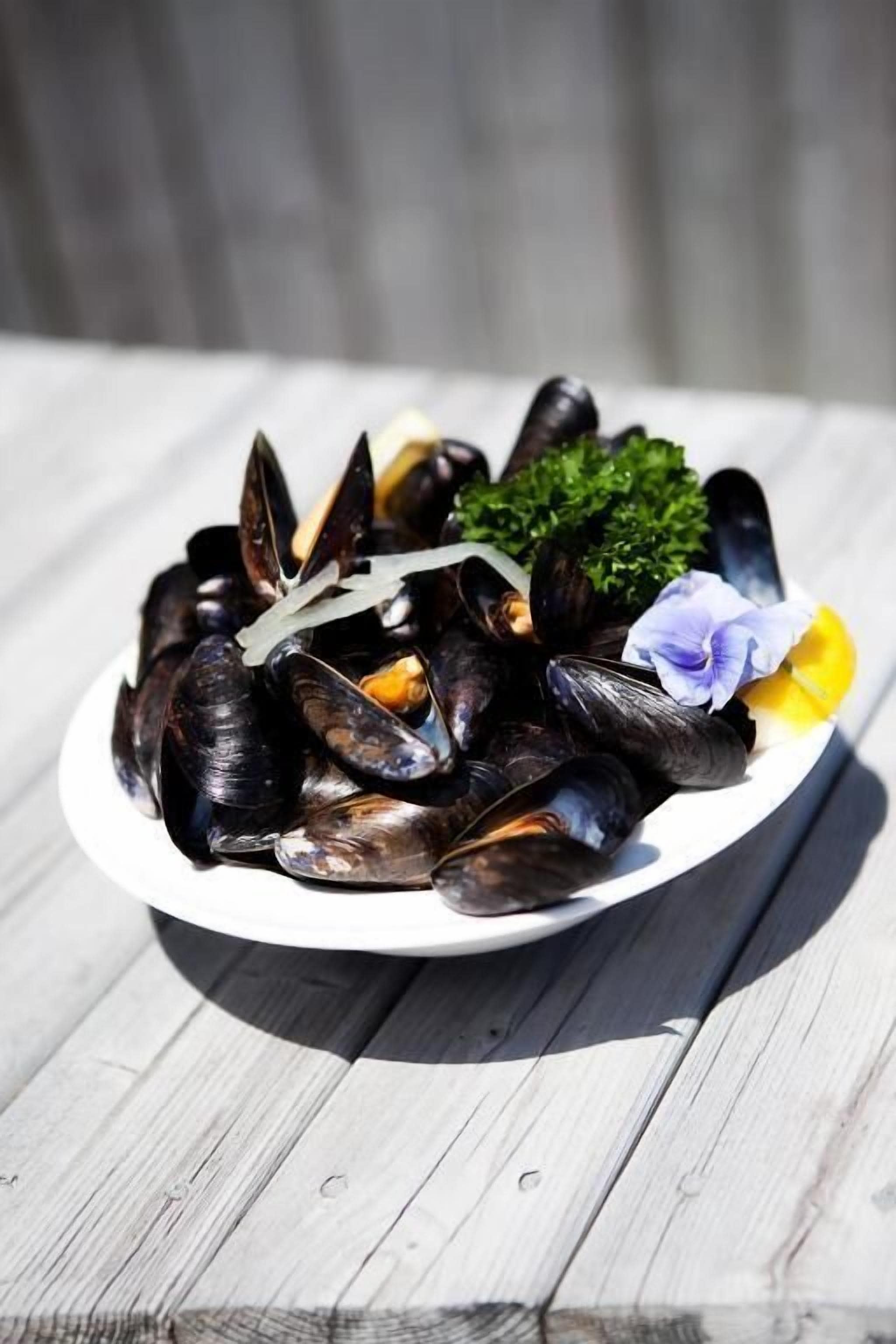 A plate of mussels with parsley and flowers on a wooden table.