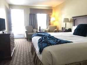 A hotel room with a bed, two armchairs, a dresser, a lamp, and a television.