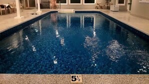 Une piscine intérieure à l’eau d’un bleu cristallin, entourée d’espaces aménagés pour s’asseoir et de plantes en pot.