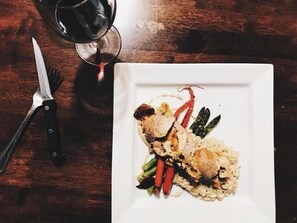 A white plate with food and a glass of red wine on a wooden table.