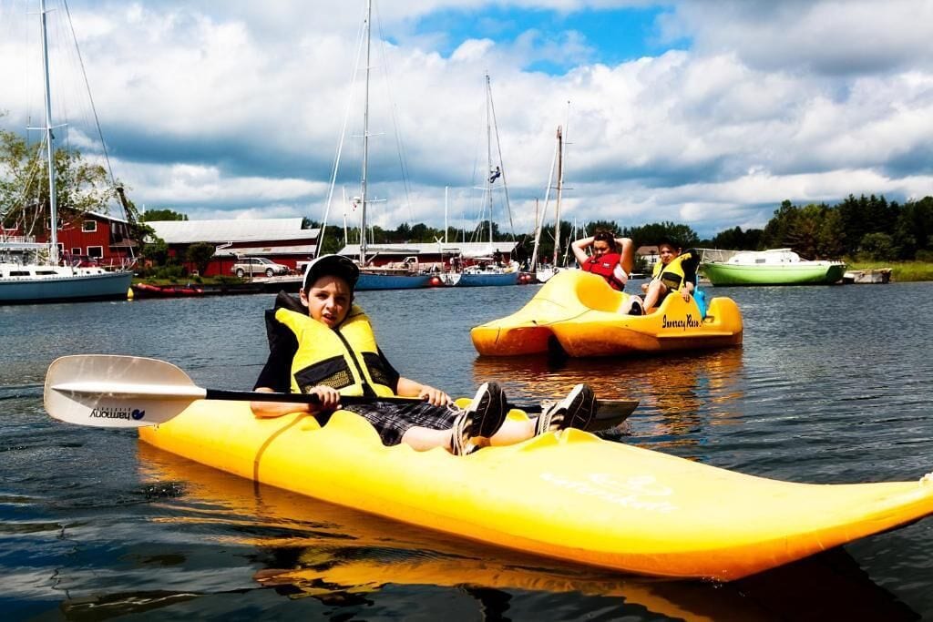 A person in a yellow kayak on a calm body of water with other kayaks and boats in the background.